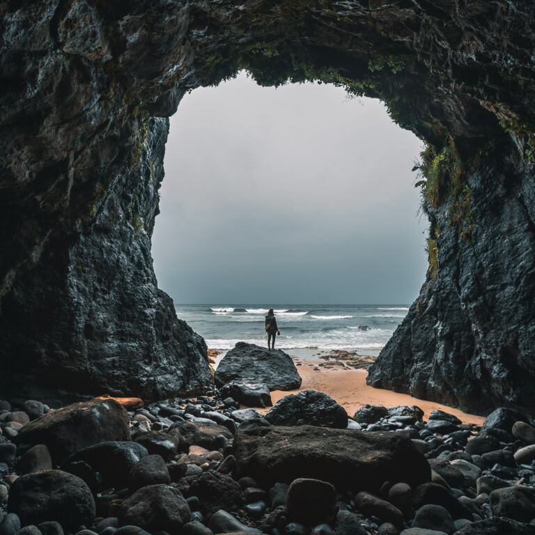 Blick aus einer Steinhöle hinaus. Der Ausgang ist riesig und vor der Höle ist das Strand und Meer zu sehen