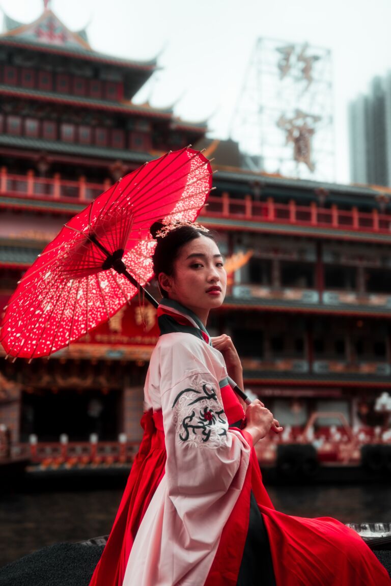 Eine rot-weiß gekleidete Japanerin mit einem rotem Sonnenschirm